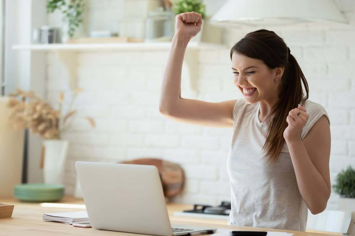 Donna che esulta felice con le braccia alzate di fronte il PC