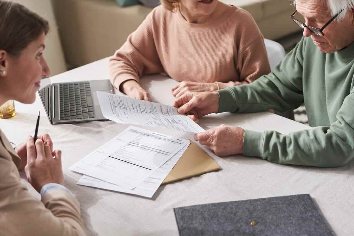 Coppia di anziani con fogli di carta (documenti), e di fronte a loro una donna in consulenza