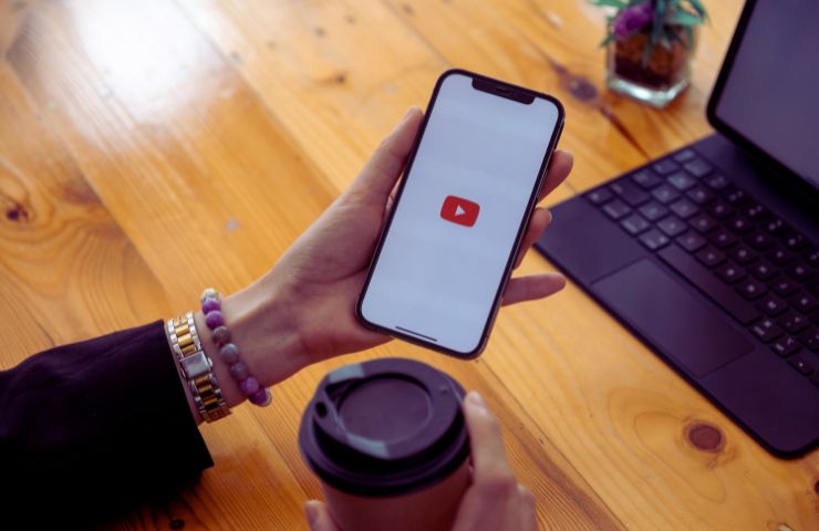 donna tiene in mano uno smartphone con logo di YouTube